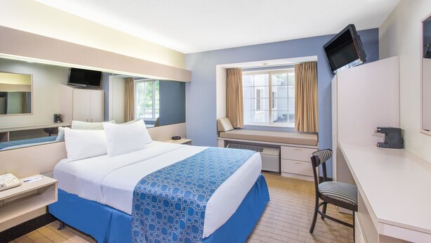 A hotel room with a bed, desk, chair, TV, and a window with curtains.