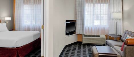 A hotel room with a bed, a TV, a sofa, a table, and a window with curtains.