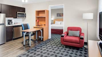 Een hotelkamer met kitchenette, bureau met stoel, rode bank, bed en televisie.