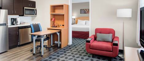 Quarto de hotel com cozinha compacta, escrivaninha com cadeira, sofá vermelho, cama e televisão.