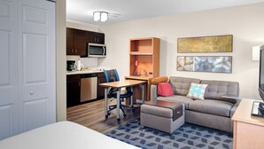 A hotel room with a bed, a desk with a chair, a sofa, a microwave, a coffee maker, and a painting on the wall. - TownePlace Suites by Marriott Wichita East (Wichita)