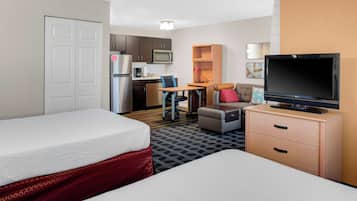 A hotel room with two beds, a kitchenette, a TV, and a desk with a chair.