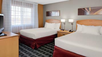 A hotel room with two beds, a desk, a TV, and a window with curtains.