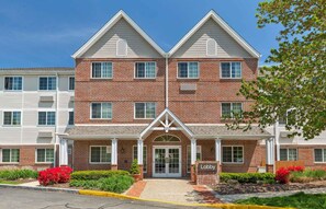A two-story brick building with a central entrance, a sign reading "Lobby," and a small garden area with red flowers. - Extended Stay America Suites Boston Peabody (Peabody)