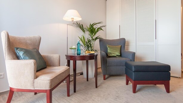 A modern living room with two armchairs, a small side table with a lamp, and a large closet. - AKZENT Hotel Löwen (Langenargen)