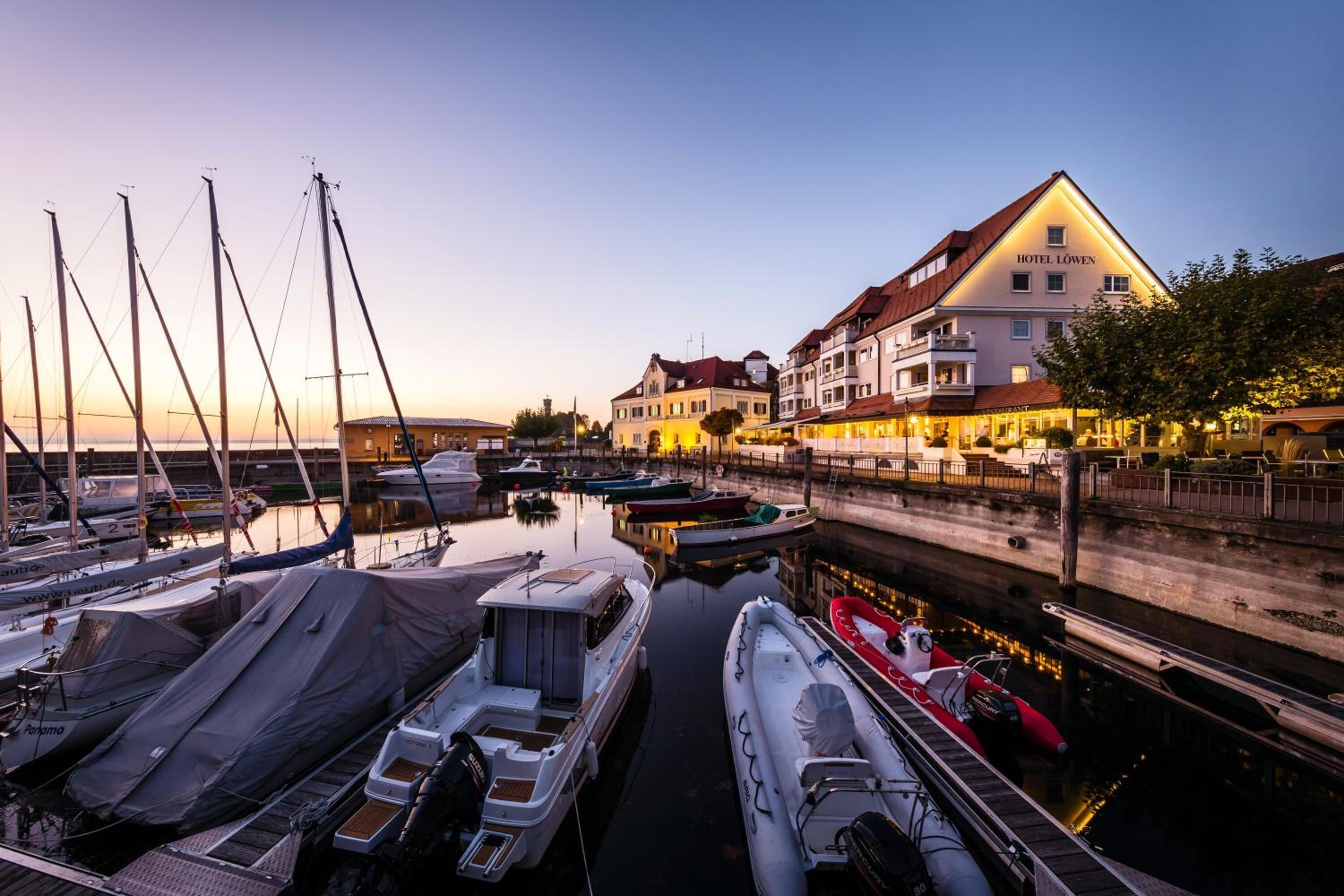 Een jachthaven met aangemeerde boten, een hotel genaamd Hotel Löwen, en een rustige waterkant.