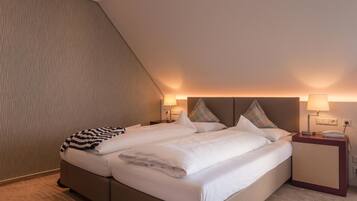 A modern hotel room with a large bed, two bedside tables with lamps, and a sloped ceiling.