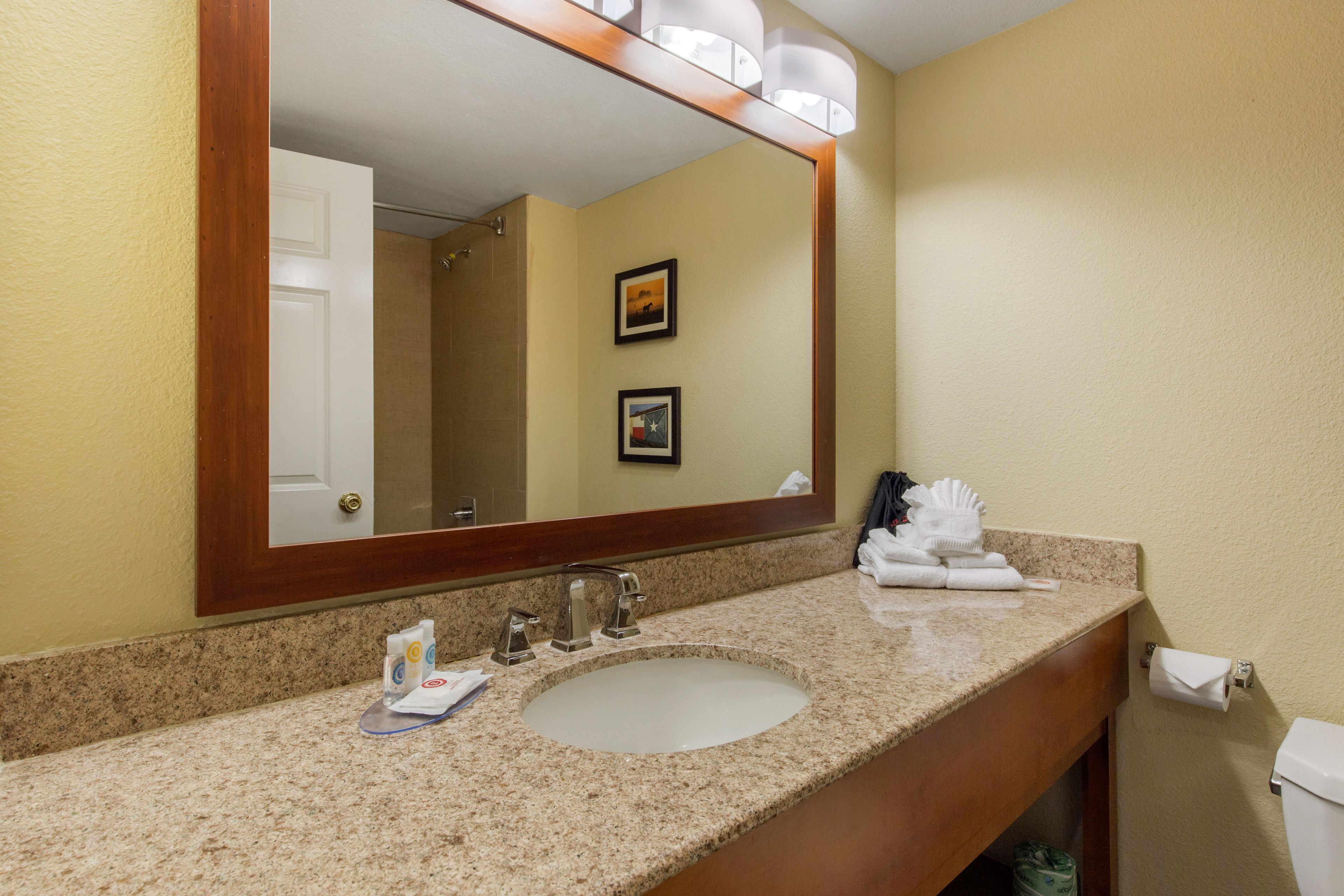 A hotel bathroom with a granite countertop sink, a large mirror, and a toilet.