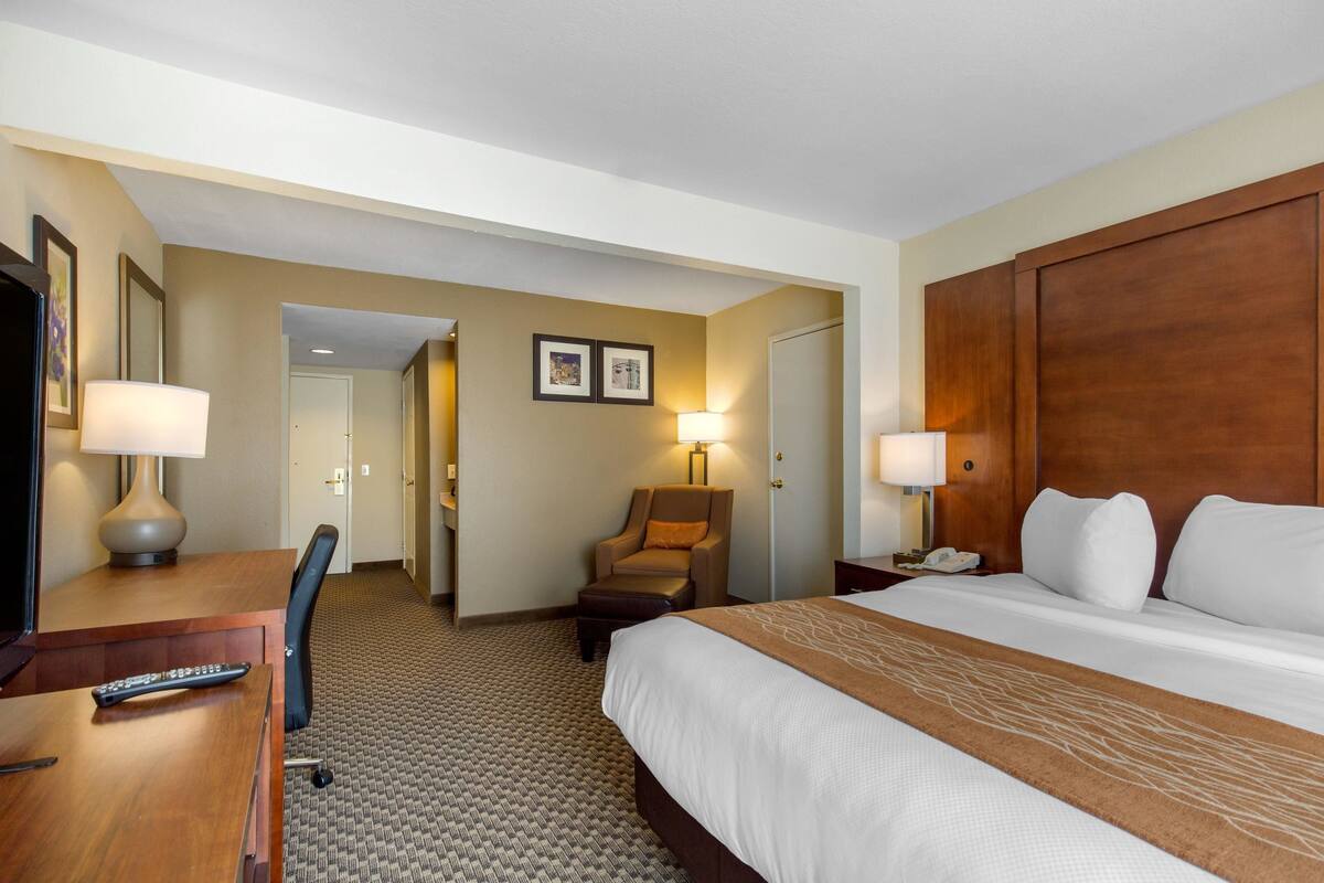 A hotel room with a large bed, a desk with a lamp, a chair, and a nightstand with a phone.