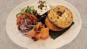 A white plate with a bagel, smoked salmon, capers, and a salad.