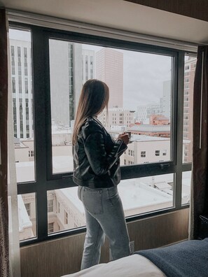 A person standing by a window with a cityscape view.