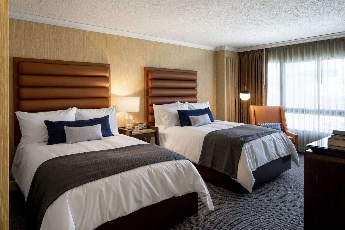 A hotel room with two beds, a desk, and a chair.