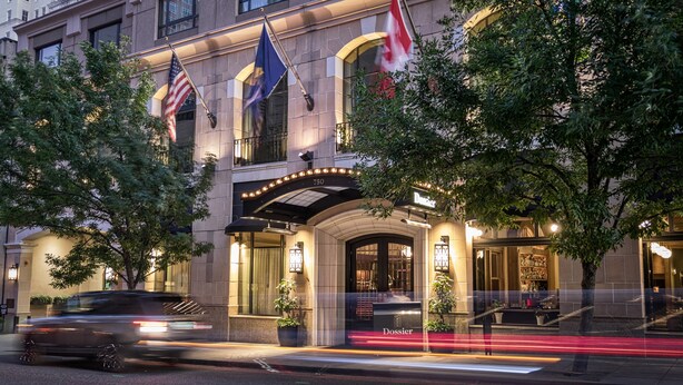 A hotel entrance with flags, a sign reading "Dossier," and a well-lit facade. - Dossier Hotel (Portland)