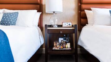 Habitación de hotel con dos camas, una mesita de noche con lámpara y una mesa con aperitivos y bebidas.