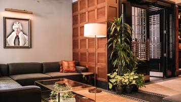A modern lobby with a leather sofa, a glass coffee table, a large floor lamp, and a potted plant.