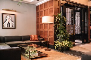 Un moderno hall de entrada con un sofá de cuero, una mesa de centro de vidrio, una lámpara de pie grande y una planta en maceta.