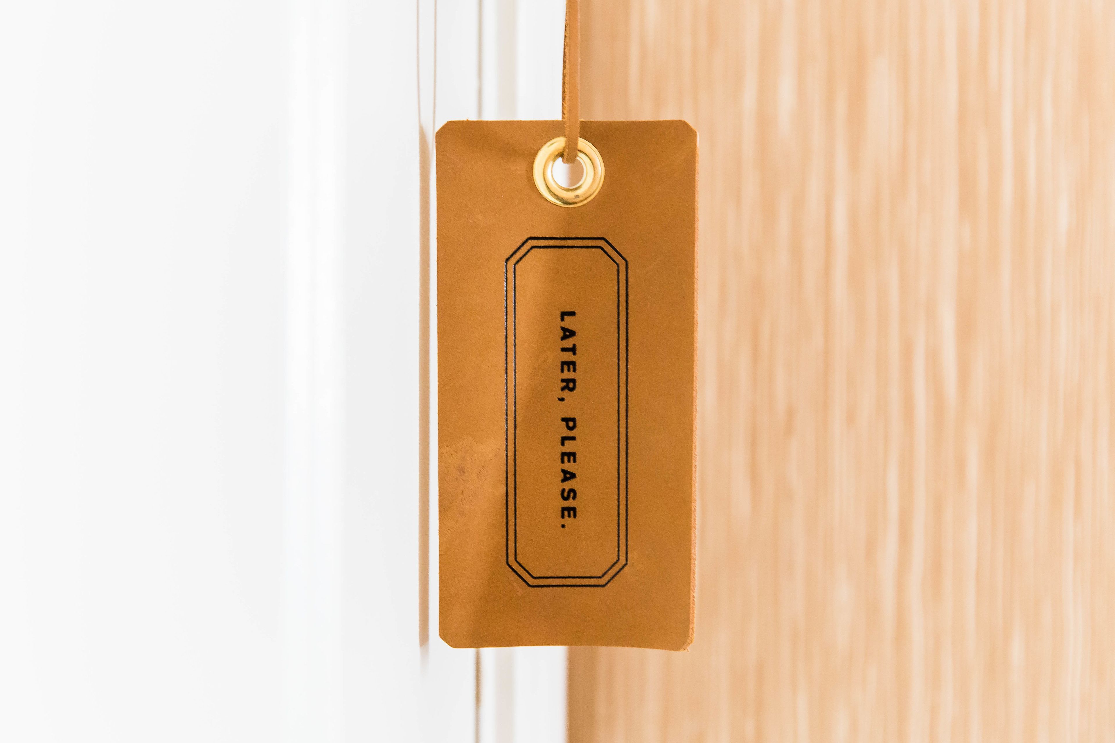 A brown tag with the text "LATER. PLEASE." hanging on a white door.