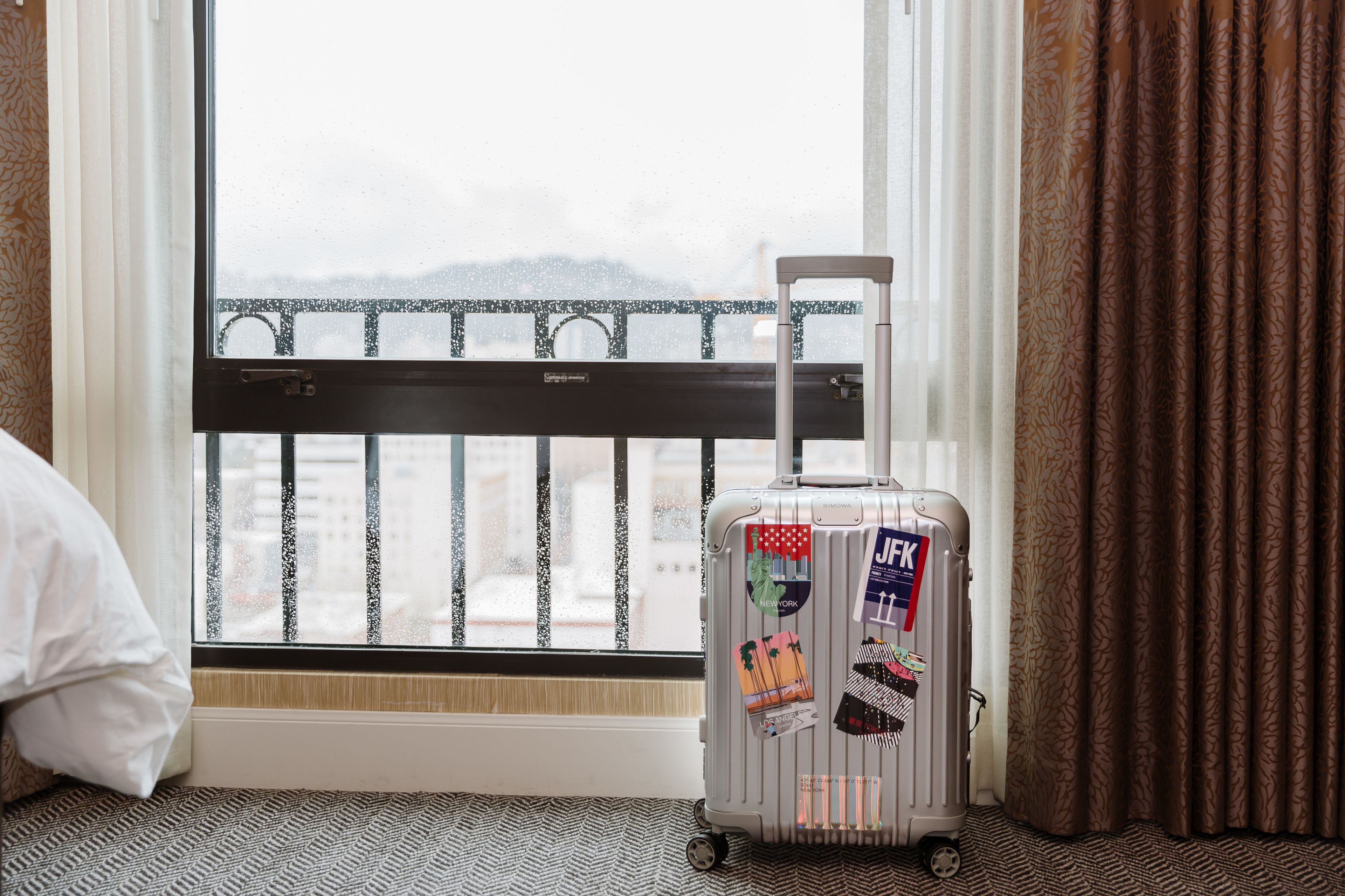 Una habitación con ventana, maleta y cama.