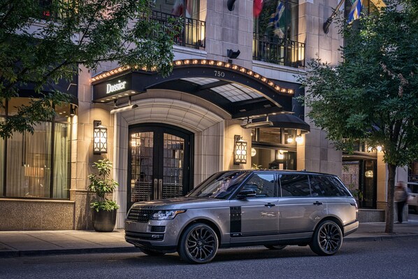 A luxury hotel entrance with a prominent address sign, a well-lit facade, and a parked Range Rover SUV.