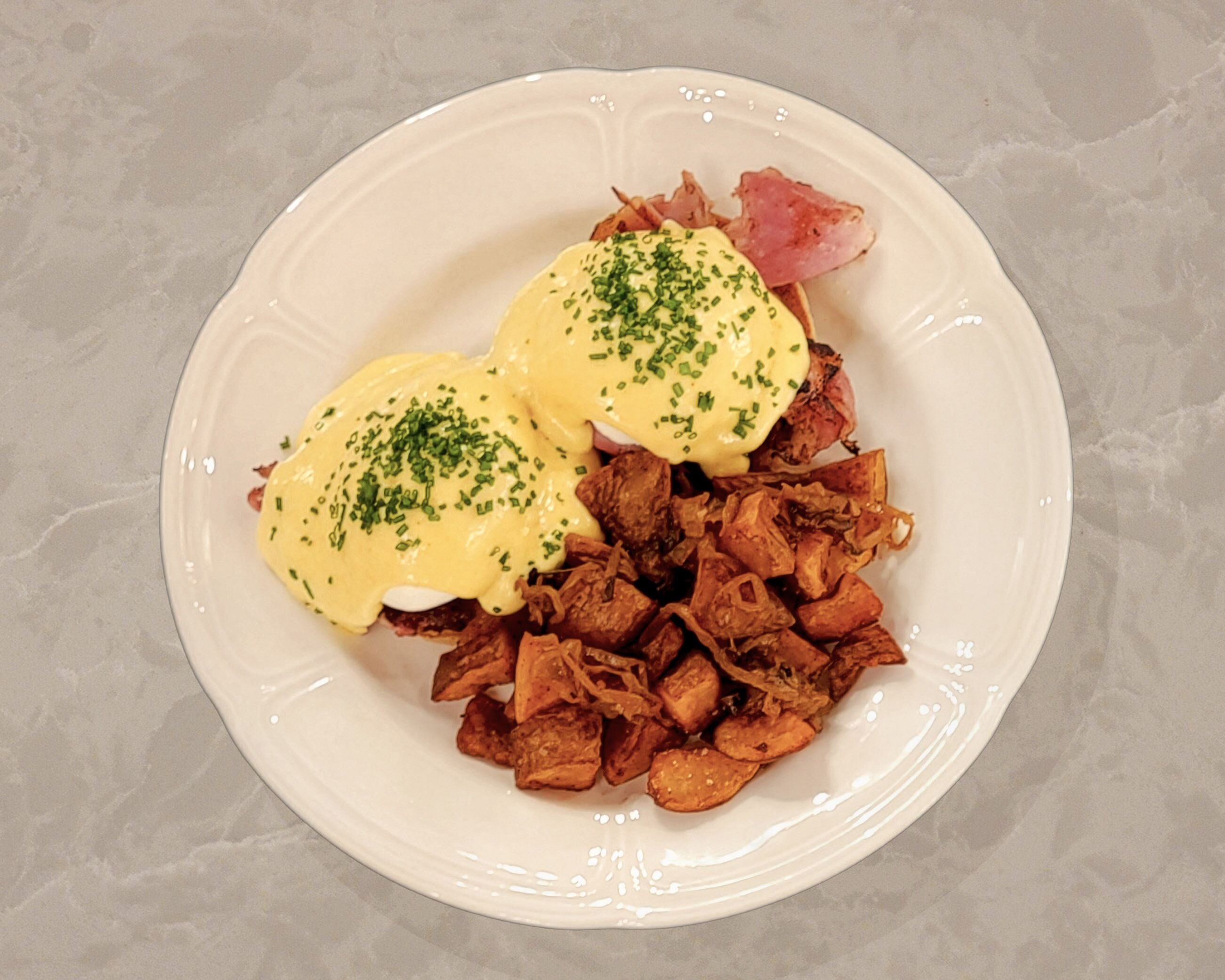 A plate of food with eggs benedict and fried potatoes.