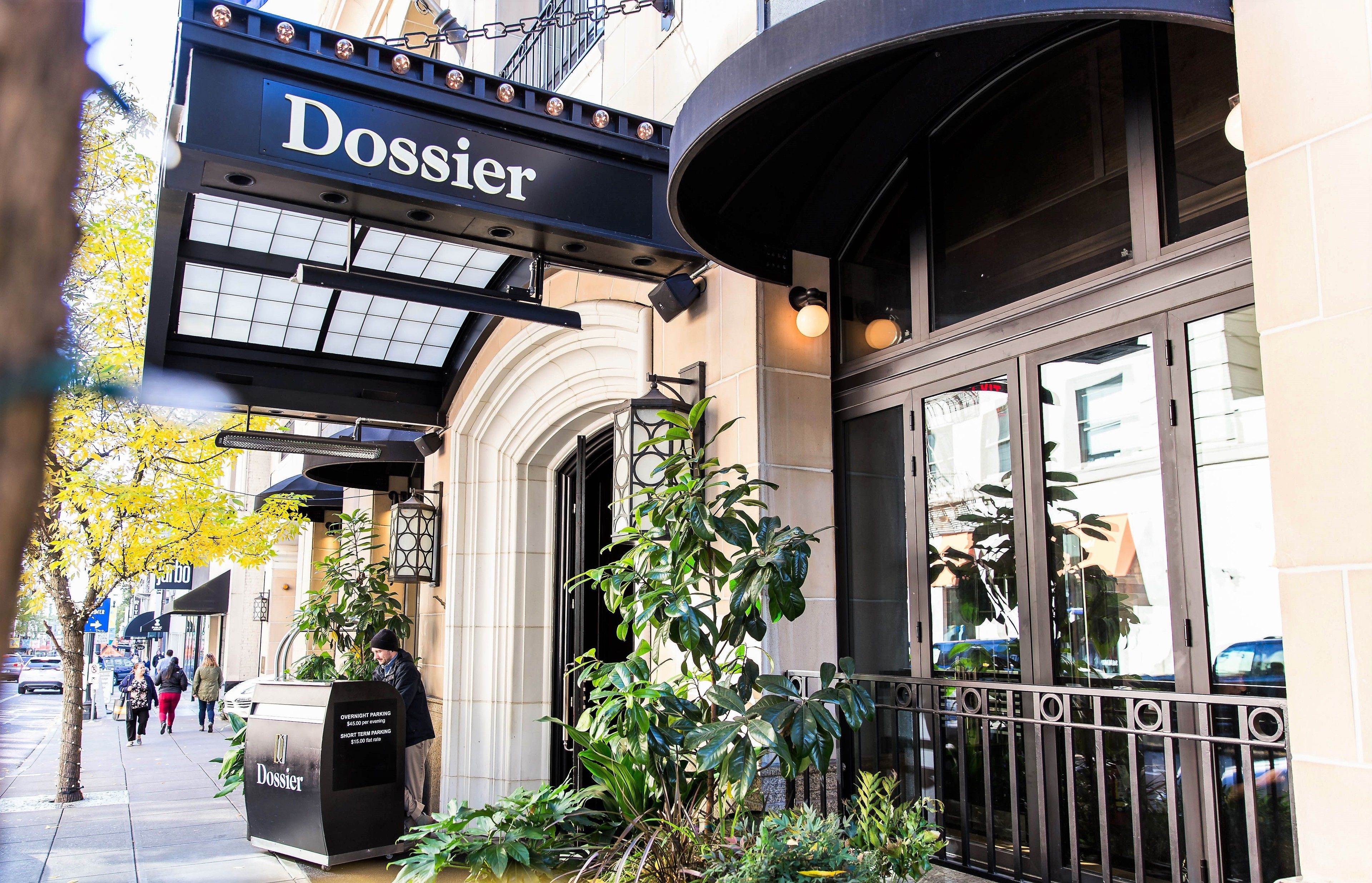 A building with a 'Dossier' sign, large windows, and a planter with green plants.