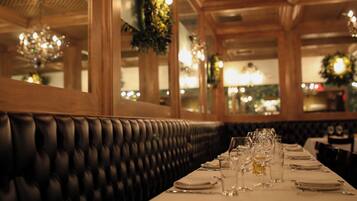 A restaurant with a long table set for dining, featuring a black upholstered bench and a chandelier.