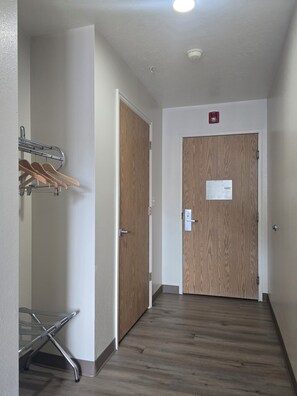 A hallway with a coat rack, two wooden doors, and a metal chair. - Economy Inn (Nephi)