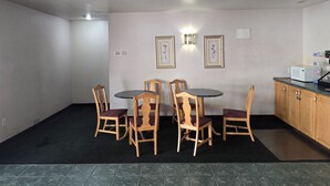 A dining area with a round table and four wooden chairs, a kitchen with a microwave, and a sign indicating room numbers. - Economy Inn (Nephi)