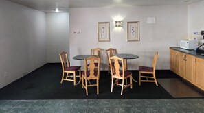 A dining area with a round table and four wooden chairs, a kitchen with a microwave, and a sign indicating room numbers. - Economy Inn (Nephi)