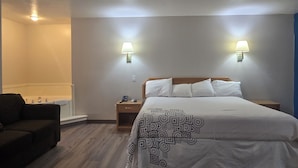 A hotel room with a bed, bedside tables, a lamp, a sofa, and a bathroom. - Economy Inn (Nephi)