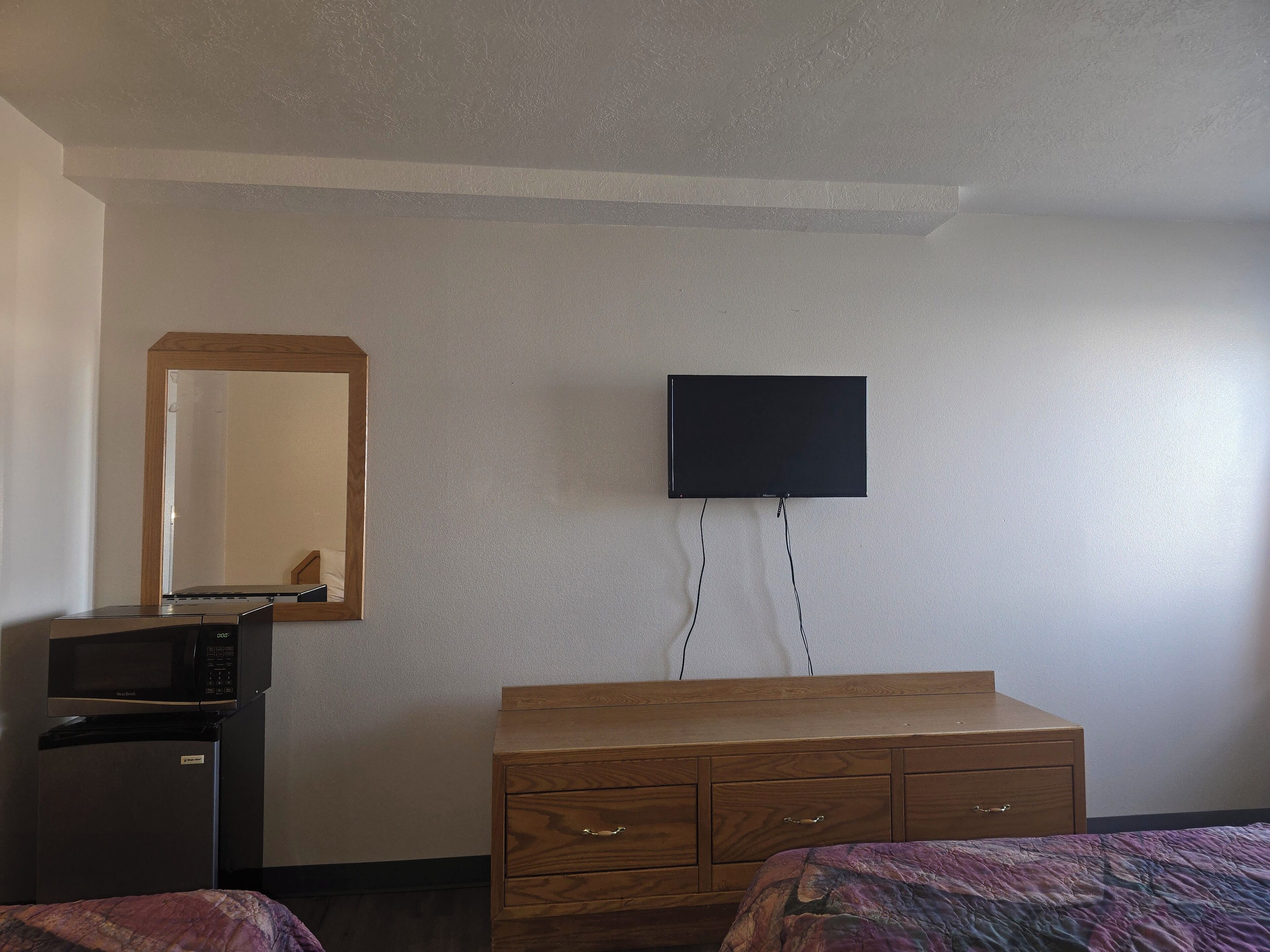 Een hotelkamer met een flatscreen televisie aan de muur, een houten dressoir, een magnetron en een koelkast.