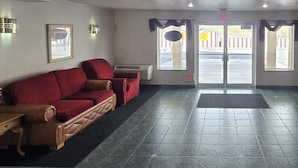 A hotel lobby with a red sofa, a wooden table with chairs, and a tiled floor. - Economy Inn (Nephi)