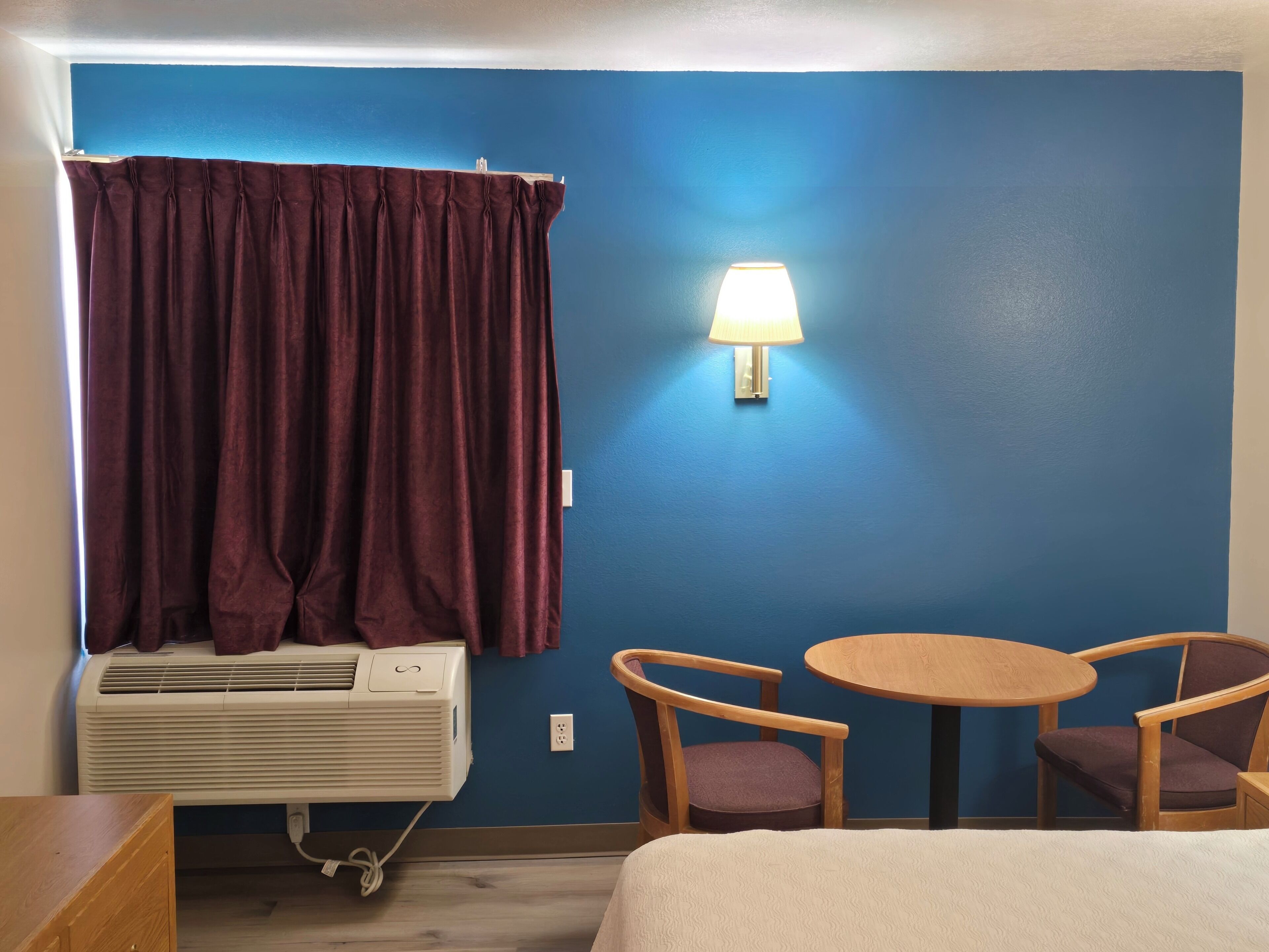 Una habitación con una cama, una mesa con dos sillas, una lámpara de pared y un aire acondicionado.
