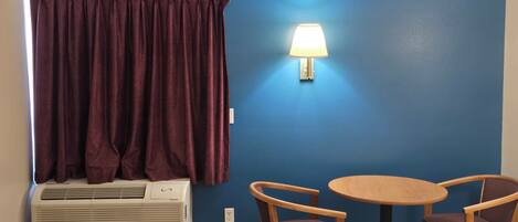 Una habitación con una cama, una mesa con dos sillas, una lámpara de pared y un aire acondicionado.