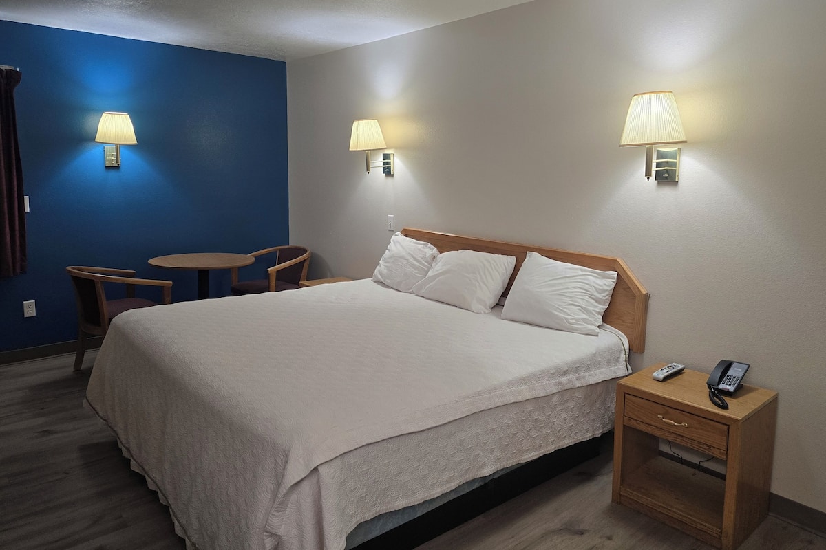 A hotel room with a bed, bedside table, lamp, and a small table with chairs.