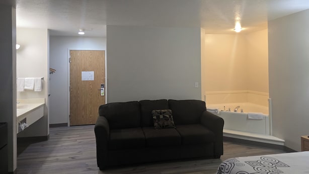 A room with a sofa, a bed, a bathroom with a bathtub, and a wooden door. - Economy Inn (Nephi)