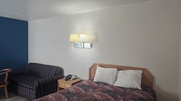 A hotel room with a bed, a chair, a nightstand, and a wall-mounted lamp.