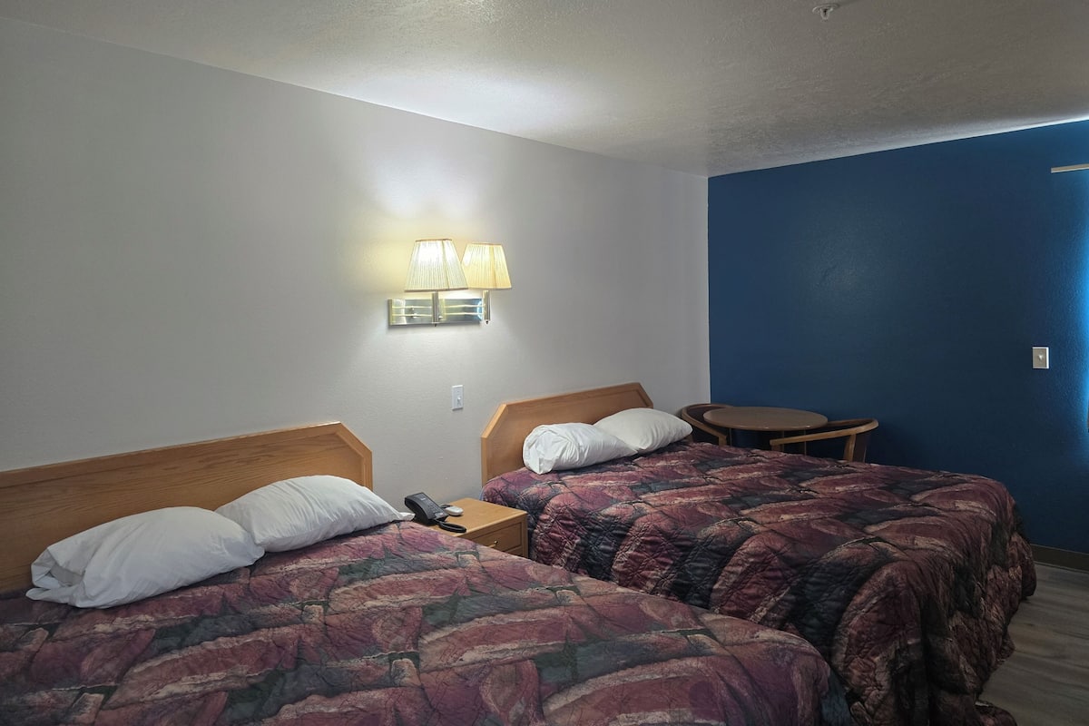 A hotel room with two beds, a nightstand with a phone, a lamp, and a small table.