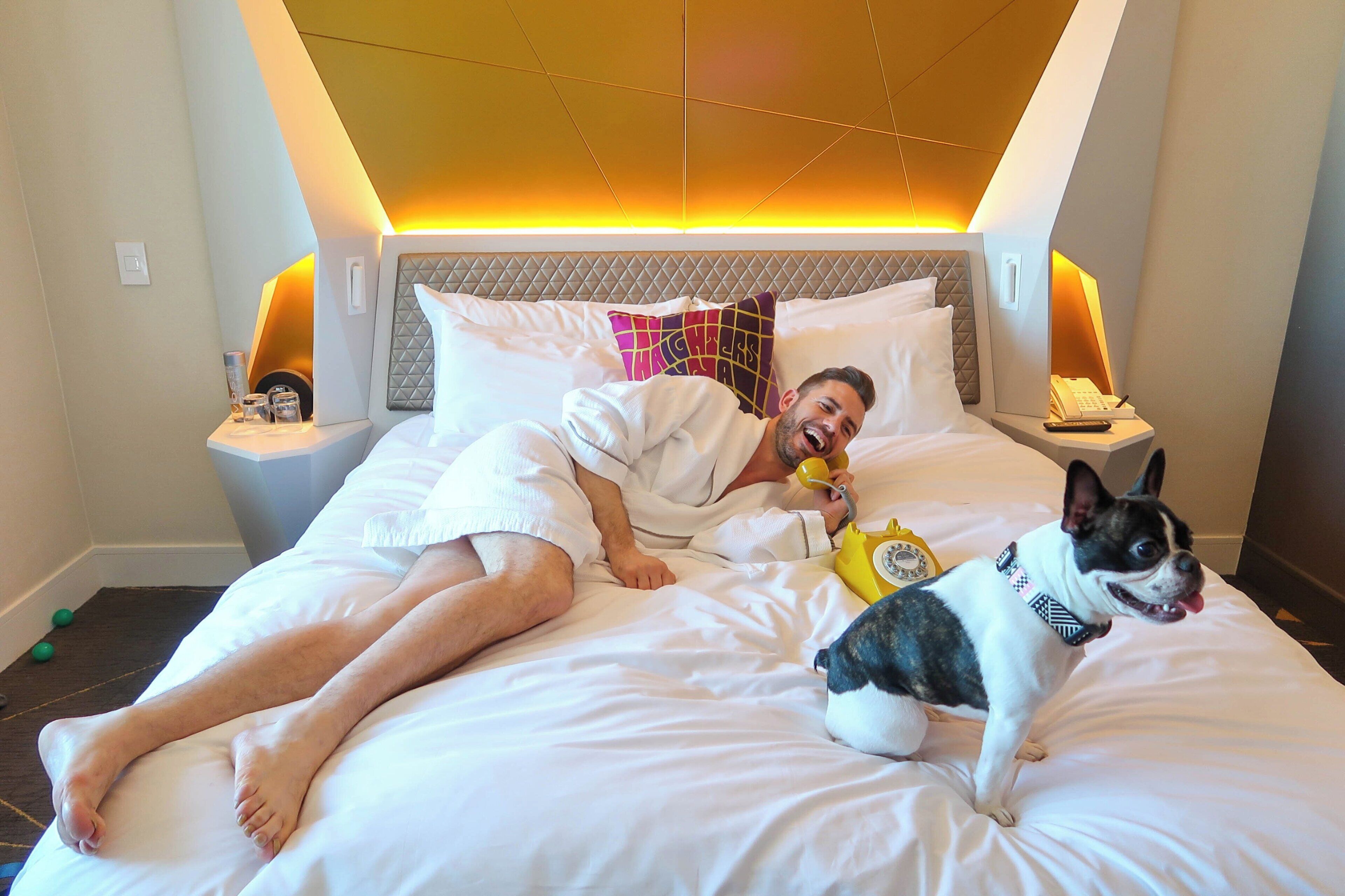 Una cama con cabecera, almohadas y mesita de noche con una lámpara y un teléfono.