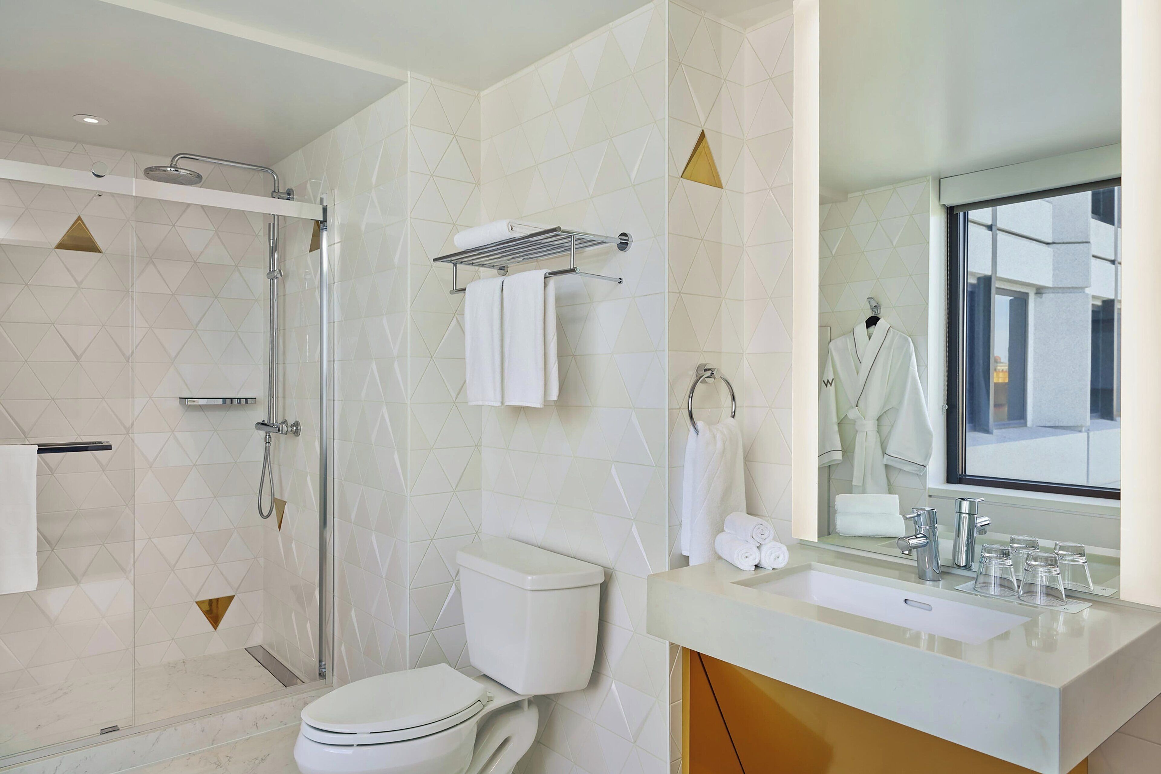 Un baño moderno con ducha de vidrio, inodoro, lavamanos con espejo y toallero.