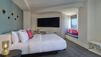 Quarto de hotel moderno com uma cama grande, uma TV de tela plana na parede, uma escrivaninha e uma janela com vista para a cidade.