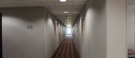 Un pasillo largo y estrecho con piso estampado, paredes blancas y puertas a ambos lados.