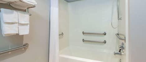 Un baño con ducha a nivel, barras de apoyo y un perchero con toallas dobladas.