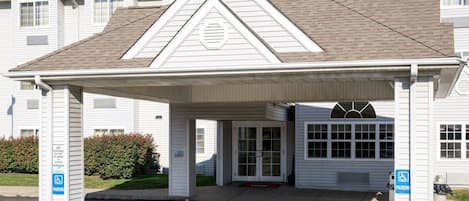 A white building with a covered entrance, a parking area, and a handicap parking sign.