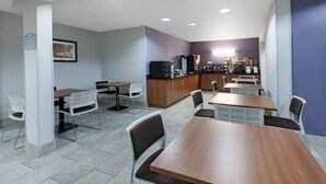 A modern dining area with multiple tables and chairs, a kitchen area with a refrigerator and coffee machines, and a sign indicating a smoking area. - Microtel Inn & Suites by Wyndham Pittsburgh Airport (Pittsburgh)
