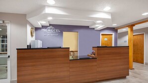 A reception desk with a wooden finish and a glass top, a sign above it reading "MICROTEL INN & SUITES BY WYNDHAM", and a door to the right. - Microtel Inn & Suites by Wyndham Pittsburgh Airport (Pittsburgh)