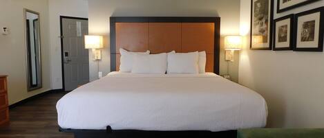 Quarto de hotel com uma cama grande, duas luminárias de cabeceira, um painel de cabeceira de madeira e quadros decorativos nas paredes.