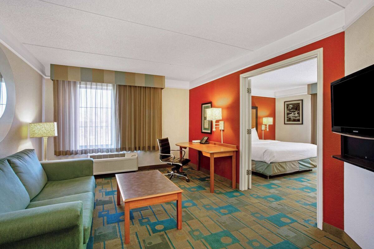 A hotel room with a bed, a desk, a chair, a sofa, and a television.