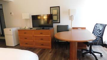Una habitación de hotel con cama, cómoda de madera, televisión, escritorio con silla y lámpara.