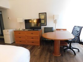 Una habitación de hotel con cama, cómoda de madera, televisión, escritorio con silla y lámpara.